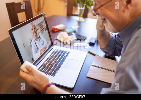 Ein älterer Mann, der sich mit einem Arzt auf seinem Laptop beraten hat Stockfoto