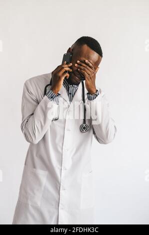Serious verwirrt afroamerikanischen Arzt am Telefon zu sprechen. Der Arzt erhielt schlechte Nachrichten und hoffte auf ein positives Ergebnis. Weißer Hintergrund Stockfoto