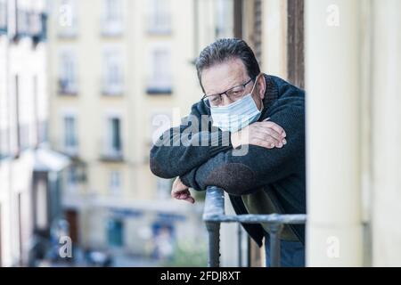 Covid-19 Lockdown und Angst - trauriger und depressiver reifer Mann 65 - 70 Jahre alt in Virusschutzmaske bei Home Balkon einsam verängstigt Blick weg Stockfoto