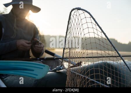 Netz zum Herausziehen von Fischen aus dem Wasser in einem aufblasbaren Boot, vor einem verschwommenen Hintergrund, bereitet sich ein Fischer im Morgengrauen auf das Fischen vor. Stockfoto