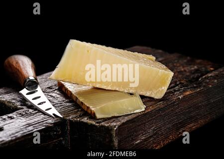 Nahaufnahme von Cheddar-Käse. Halbweicher, gereifter Kuhmilchkäse nach einem alten englischen Rezept. Stück Käse auf einem dunklen Holzbrett und Messer für Stockfoto