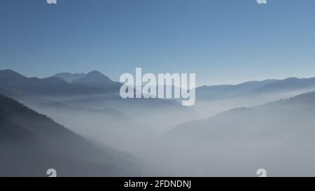 Ein Panoramablick auf Schichten von Bergen mit Nebel in Das Tal und der klare blaue Himmel Stockfoto