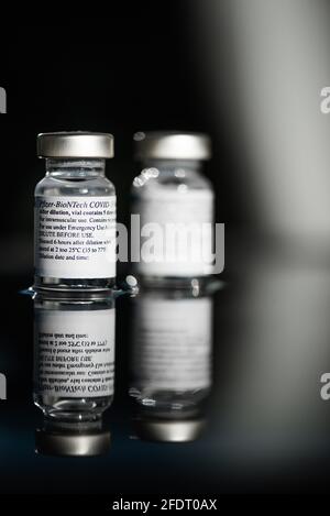 San Sebastian, Gipuzkoa, Spanien; 24. April 2021. Selektiver Fokus von zwei Vakzinoronavirus-Pfizer-Fläschchen auf schwarzem Hintergrund mit Reflexion. Stockfoto