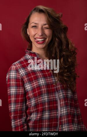 Porträt einer hübschen Frau, die Spaß hat, zeigt Zunge und Augenzwinkern Auf rotem Hintergrund Stockfoto