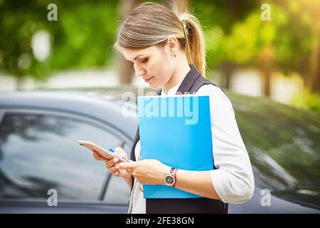 Eine junge Geschäftsfrau mit einem Ordner für Papiere in ihren Händen schaut auf ihr Smartphone. Stockfoto
