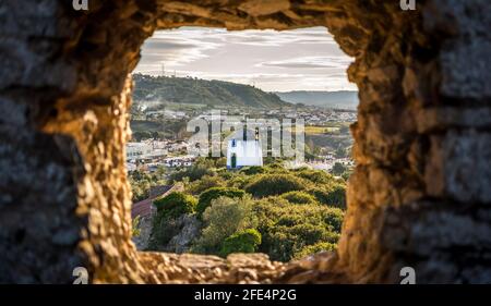 Alte Windmühle durch kleine Fenster in Obidos Festung Wand, Portugal. Abend-Sonnenlicht Stockfoto