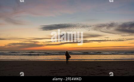 Surfen Bei Sonnenuntergang. Silhouette einer weiblichen Surferin, die Bretter am Strand entlang trägt Stockfoto