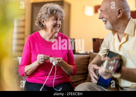 Das ältere Paar sitzt auf dem Sofa, die Frau strickte und der Mann spielte Gitarre Stockfoto