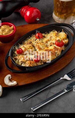 Gebackene Champignons, mit Käse, Petersilie und geröstetem Knoblauch in einer schwarzen Schüssel. Stockfoto