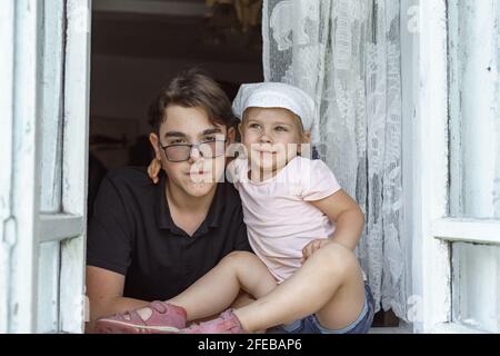 Kinder sitzen am Fenster eines Dorfhauses. Stockfoto