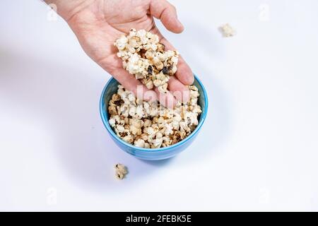 Verbrannter Popcornkern in blauer Tasse, Menschenhand nimmt Popcorn Stockfoto