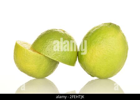 Eine ganze und zwei Hälften einer saftigen Limette, Nahaufnahme, vor weißem Hintergrund. Stockfoto