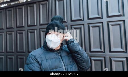 Älterer Mann mit Hut und blauem Mantel, der eine aufsetzt Weiße Maske im Freien Stockfoto