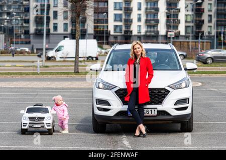 Riga, Lettland - 16. April 2021: Mutter und ihre kleine Tochter mit ihren weißen Autos, Konzept verschiedener Generationen Stockfoto