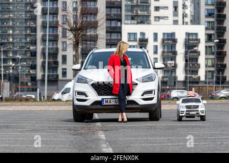 Riga, Lettland - 16. April 2021: Mutter und ihre kleine Tochter mit ihren weißen Autos, Konzept verschiedener Generationen Stockfoto