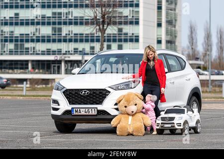 Riga, Lettland - 16. April 2021: Mutter und ihre kleine Tochter mit ihren weißen Autos, Konzept verschiedener Generationen Stockfoto