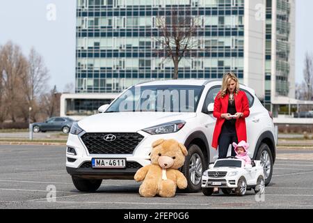 Riga, Lettland - 16. April 2021: Mutter und ihre kleine Tochter mit ihren weißen Autos, Konzept verschiedener Generationen Stockfoto