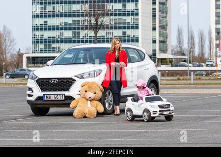 Riga, Lettland - 16. April 2021: Mutter und ihre kleine Tochter mit ihren weißen Autos, Konzept verschiedener Generationen Stockfoto