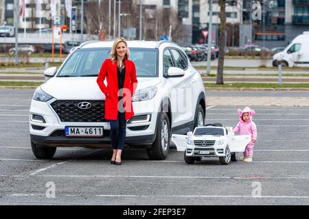 Riga, Lettland - 16. April 2021: Mutter und ihre kleine Tochter mit ihren weißen Autos, Konzept verschiedener Generationen Stockfoto