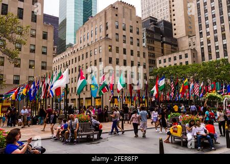 Touristen, die an einem Sommertag am Rockefeller Center an den Flaggen sitzen und spazieren gehen Stockfoto