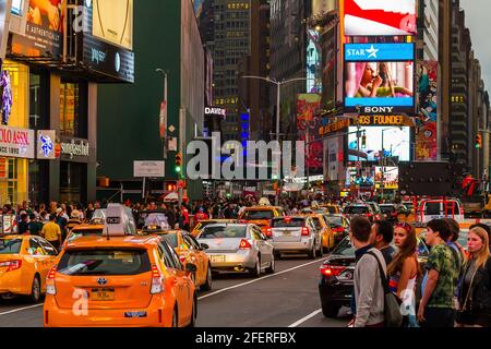 Starker Verkehr mit Autos, Taxis und Touristen, die vorbeifahren Die Straße an einem geschäftigen Abend am Times Square Stockfoto