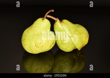 Eine ganze und zwei Hälften aus organischer grüner Birne, Nahaufnahme, isoliert auf Schwarz. Stockfoto