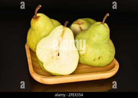 Eine Hälfte und ein paar ganze süße Birnen auf einem Bambusblech. Der Hintergrund ist schwarz. Stockfoto