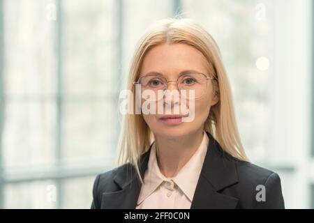 Porträt von ernst schönen reifen Exekutive in runden Brille stehend Gegen das Bürofenster Stockfoto