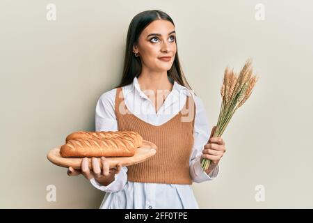 Schöne Brünette junge Frau hält hausgemachtes Brot und Spike Weizen lächelnd Blick zur Seite und starrte weg denken. Stockfoto