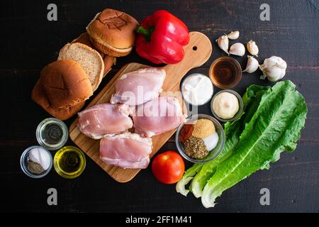 Portugiesischer Chicken Burger Zutaten: Rohe Hähnchenschenkel, Hamburger-Brötchen, Gemüse und Gewürze auf Holzboden Stockfoto
