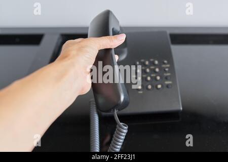 Telefon in einem Hotelzimmer, Hand mit einem erhöhten Telefonhörer aus der Nähe Stockfoto