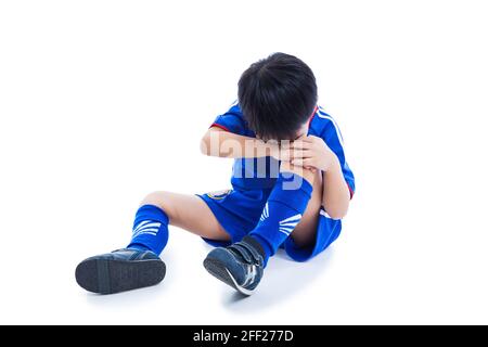 Sportverletzung. Junger asiatischer (thailändischer) Fußballspieler in blauer Uniform mit Knieschmerzen. Isoliert auf weißem Hintergrund. Studioaufnahme. Ganzkörper. Junge, der ein sitzt Stockfoto