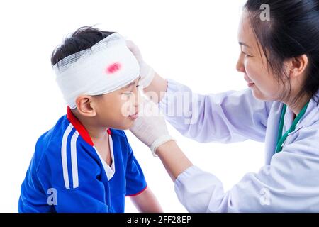 Sportverletzung. Athlet kleiner asiatischer (thailändischer) Junge in blauer Sportkleidung mit Trauma des Kopfes, blutig auf Verbandsweinung. Doktor macht Verband auf Kopf pati Stockfoto