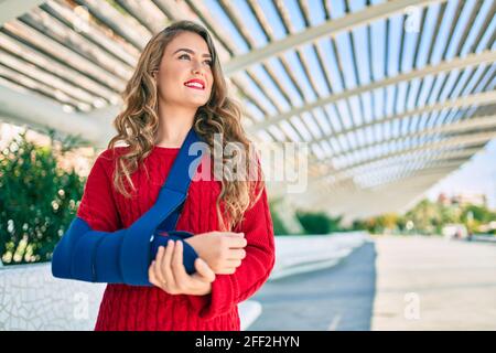 Junge blonde Mädchen lächelnd glücklich verletzt mit Arm Sling stehen im Park. Stockfoto