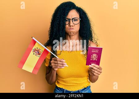 Mittlere Alter afroamerikanische Frau hält spanien Flagge und Pass Puffing Wangen mit lustigen Gesicht. Mund mit Luft aufgeblasen, Luft fangen. Stockfoto