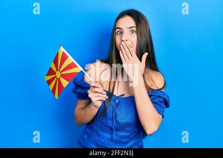 Junge Brünette Teenager hält mazedonische Flagge über den Mund mit der Hand, schockiert und Angst vor Fehlern. Überraschter Ausdruck Stockfoto