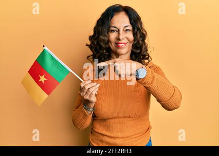 hispanische Frau mittleren Alters mit kamerunfahne lächelnd und glücklich zeigend Mit Hand und Finger Stockfoto