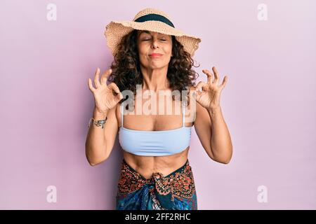 lateinamerikanische Frau mittleren Alters trägt Bikini und Sommerhut entspannen und lächeln mit geschlossenen Augen tun Meditation Geste mit den Fingern. Yoga-Konzept. Stockfoto