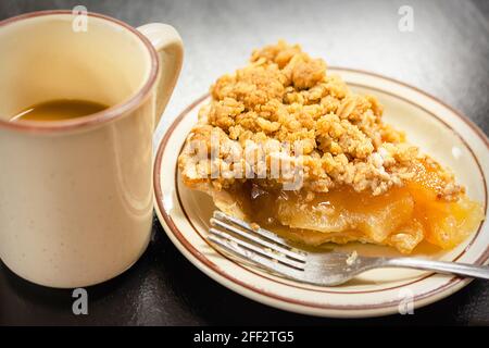 Dutch Apple Pie, Apple Crumble Pie oder Apple Streusel Pie und eine Tasse Kaffee auf einer schwarzen Theke. Stockfoto