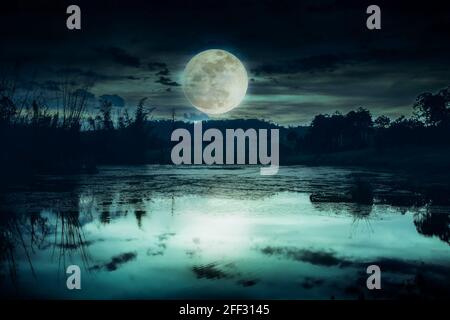 Landschaft des dunklen Nachthimmels. Schöner heller Vollmond und bewölkt über Silhouetten von Bäumen und See. Gelassenheit Natur Hintergrund. Stockfoto