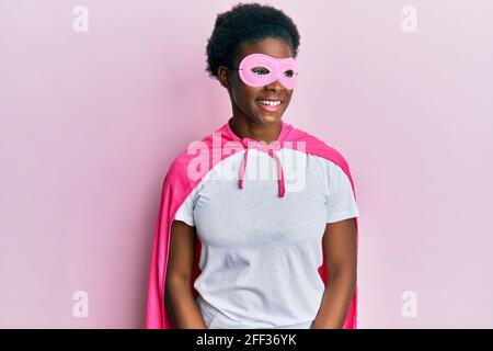 Junge afroamerikanische Mädchen trägt Superhelden-Maske und Cape Kostüm Blick weg zur Seite mit Lächeln auf Gesicht, natürlichen Ausdruck. Lachen zuversichtlich. Stockfoto