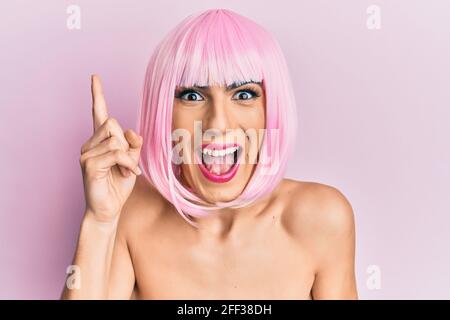 Junger Mann trägt Frau Make-up trägt rosa Perücke zeigt Finger nach oben mit erfolgreicher Idee. Begeistert und glücklich. Nummer eins. Stockfoto