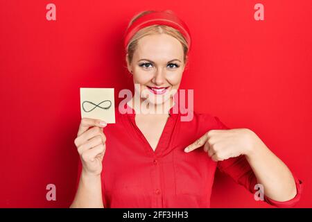 Junge blonde Frau hält unendliche Symbol Erinnerung zeigt Finger auf Ein selbst lächelt glücklich und stolz Stockfoto