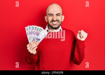 Junger kahlköpfiger Mann mit ägyptischen Pfund-Banknoten, der stolz schreit und mit erhobenem Arm den Sieg und den Erfolg feiert Stockfoto