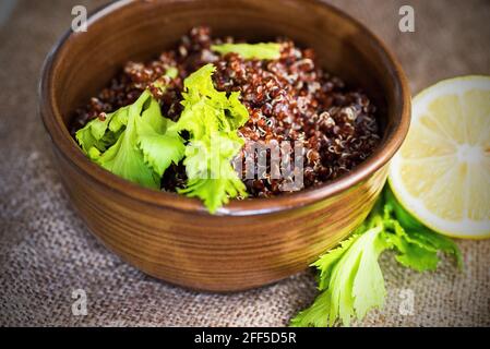 Gekochte Quinoa, sehr gesundes und glutenfreies Getreide in Keramikschale mit grünem Blatt und Zitrone auf Jute, Nahaufnahme. Stockfoto