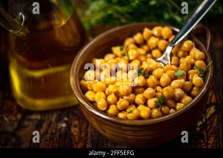 Gekochte Kichererbsen in Schüssel mit Löffel, Glaskaraffe mit Olivenöl, Kraut auf dunklem Grund, Nahaufnahme. Stockfoto