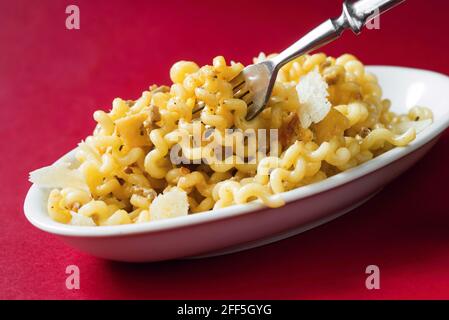 Italienische Pasta in Spiralform, Fusilli col buco, auf weißem Teller mit rustikaler Gabel, auf abfallendem roten Hintergrund, Pasta mit Parmesan und Hackfleisch Stockfoto