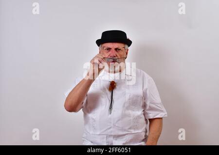 Ansicht eines älteren Mannes mit Hut und einem Weißes Hemd, das versucht, seine Brille auf Weiß zu setzen Stockfoto