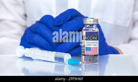 Coronavirus-Impfstoff mit USA-Flagge auf Etikett, amerikanisches Impfkonzept, Arzthände in blauen Handschuhen und Glastisch mit medizinischer Spritze Stockfoto