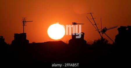 Wimbledon, London, Großbritannien. 24. April 2021. Eine klare und helle Abendsonne untergeht am orangefarbenen Himmel hinter einem Wirrwarr von Fernsehantennen auf dem Dach in den Londoner Vororten. Quelle: Malcolm Park/Alamy Live News. Stockfoto